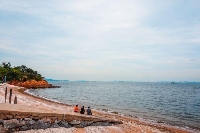 Visitors enjoying the serene beach at Muido Island, sitting on the sand and taking in the expansive ocean view.