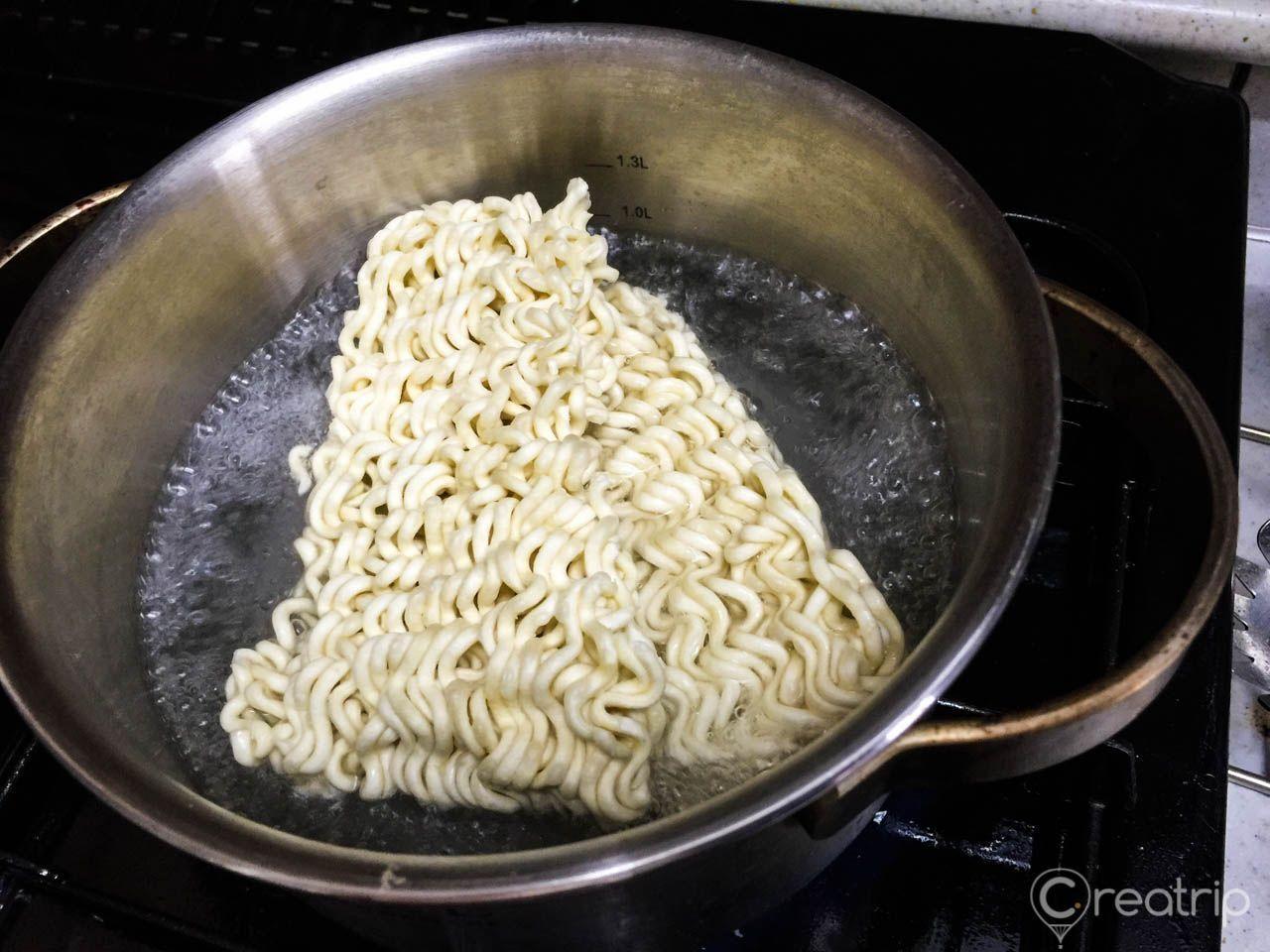 鍋中煮著正在泡的辣炒雞麵，面條輕輕浮起，水在滾沸的狀態，顯示出準備進入煮的過程。