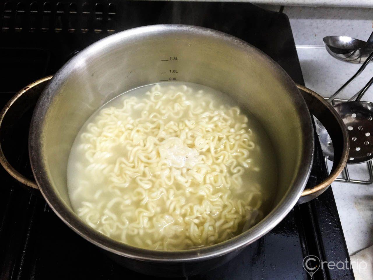 一鍋半熟的辣炒雞麵，面條膨脹且泡在熱水中，準備接下來的調味步驟。