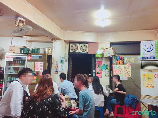 无名烧烤店内，顾客聚集在一起享用啤酒和韩式串烧。