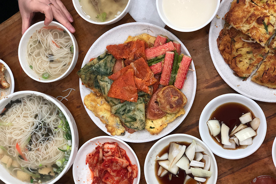 밥상 위에 놓인 다양한 족발, 파전, 그리고 잔에 담긴 막걸리. 전통 한국 음식과 잘 어울리는 조화이다.