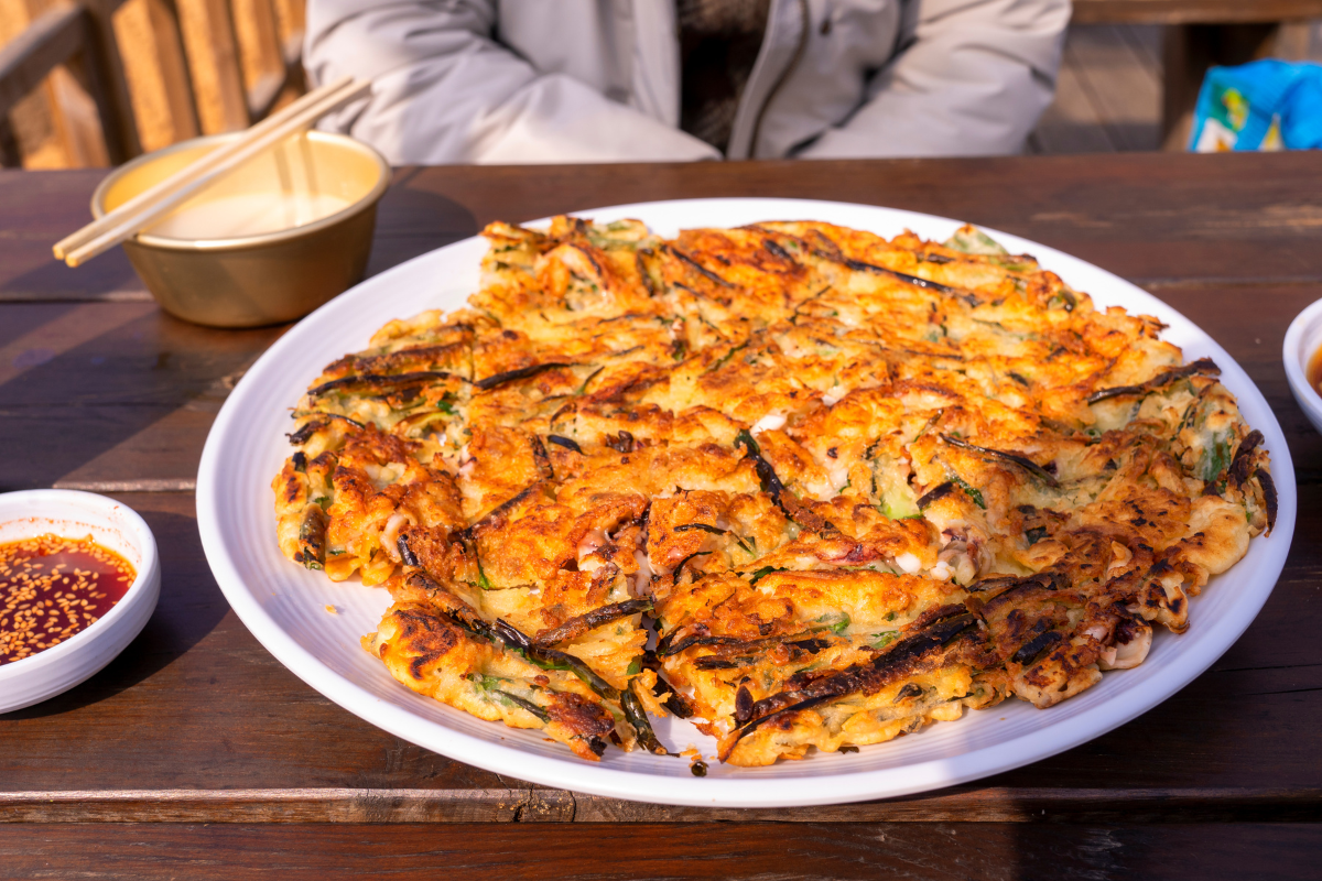 Một khay bánh xèo Hàn Quốc, pajeon, được bày trên bàn cùng với nước chấm, món ăn phổ biến khi dùng với makgeolli.
