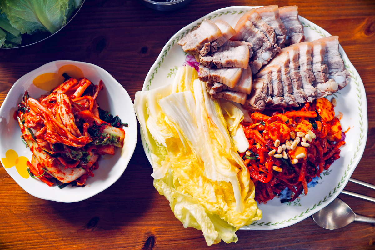 Một đĩa bossam, thịt heo luộc đậm đà với rau sống và kim chi, được sắp xếp tinh tế trên bàn.