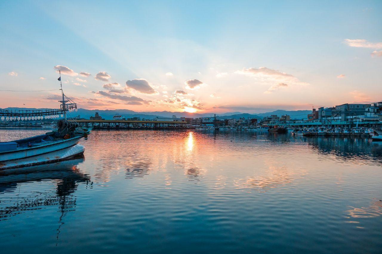 黃昏時分的港口景色，漁船停泊在水中，天邊有霞光。