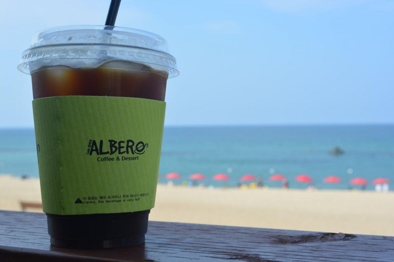 沙灘上停滿汽車，遠處海灘上有小孩在玩耍，天氣晴朗。