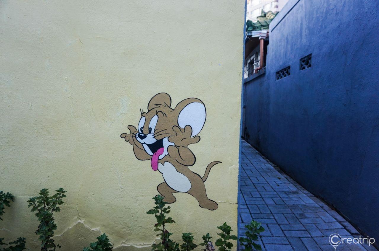 대구 옹기종기 행복마을의 벽화로 밝은 하늘과 다양한 식물이 그려진 이미지. 깔끔하고 정돈된 느낌을 줍니다.