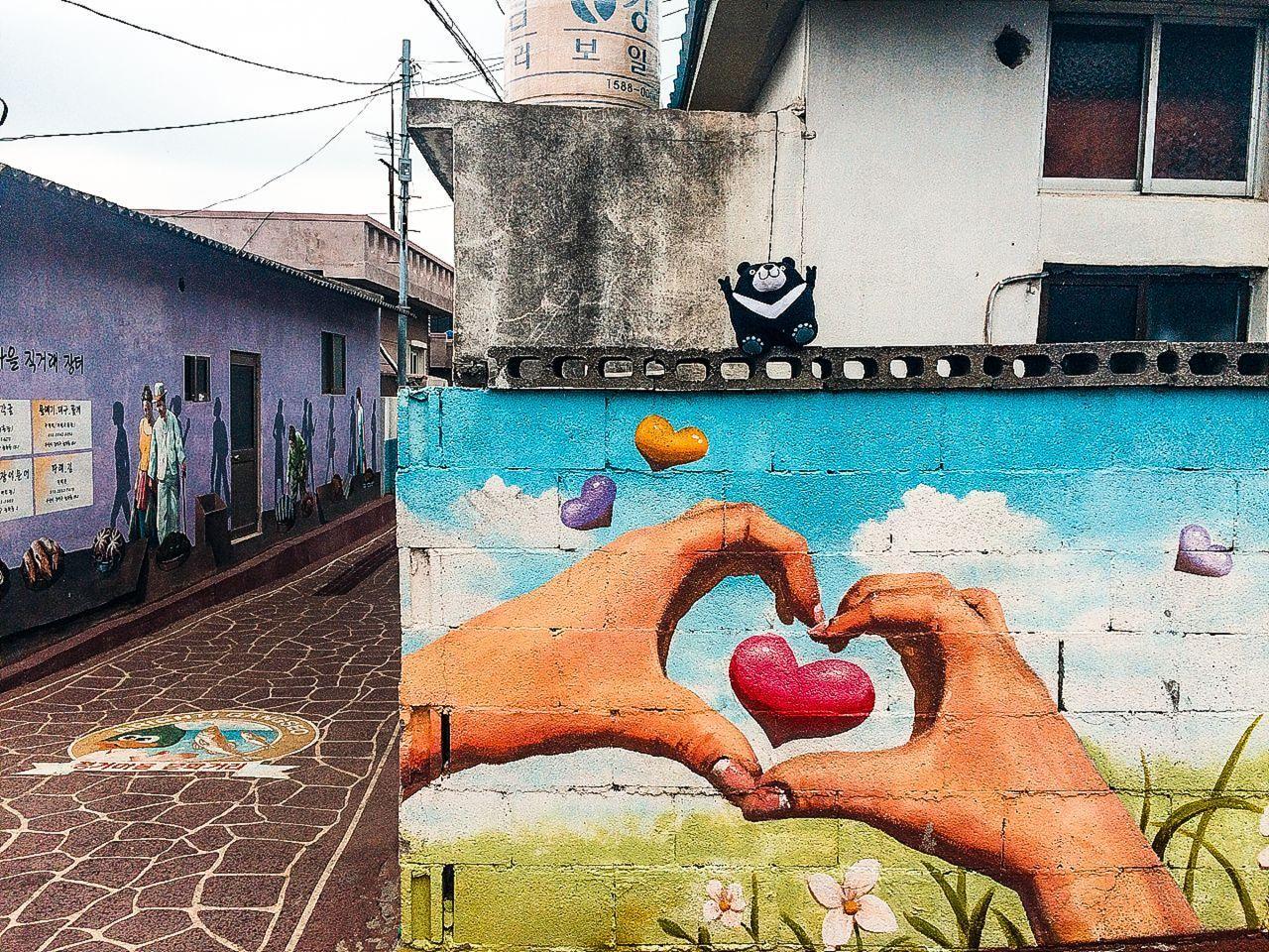 부산 가덕도 벽화마을의 고요한 항구 모습. 아침 무렵의 잔잔한 바다와 마을의 평화로운 분위기가 느껴집니다.