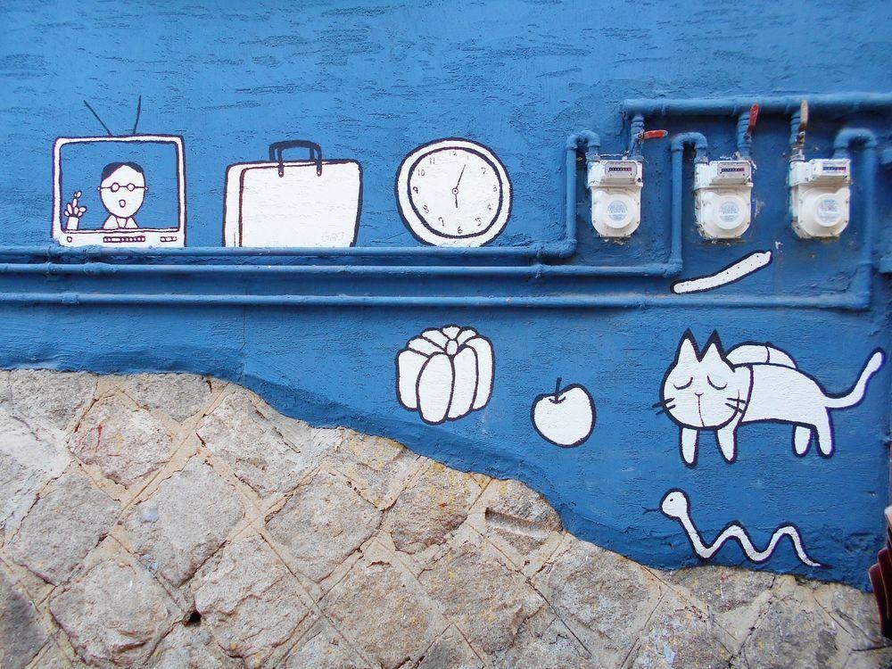 파란 벽에 소소하고 귀여운 그림들이 그려진 벽화 이미지. 작은 텔레비전, 고양이, 시계 등이 있다.