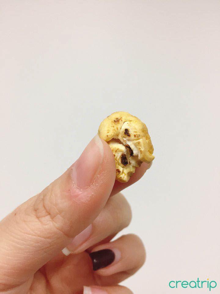 Hand holding a single popcorn piece from CU convenience store snack pack