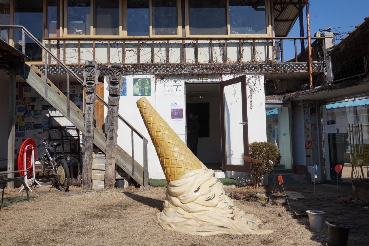 藝術空間春天外景，一個大型冰淇淋雕塑擺放在草地上，環境顯得有趣和創意。