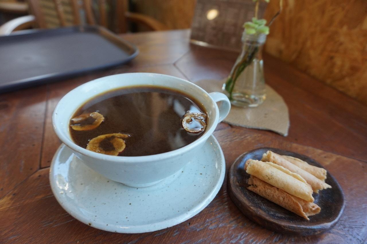 一杯熱飲和一盤小吃在木桌上，背景是溫暖的咖啡店氛圍，光線柔和。