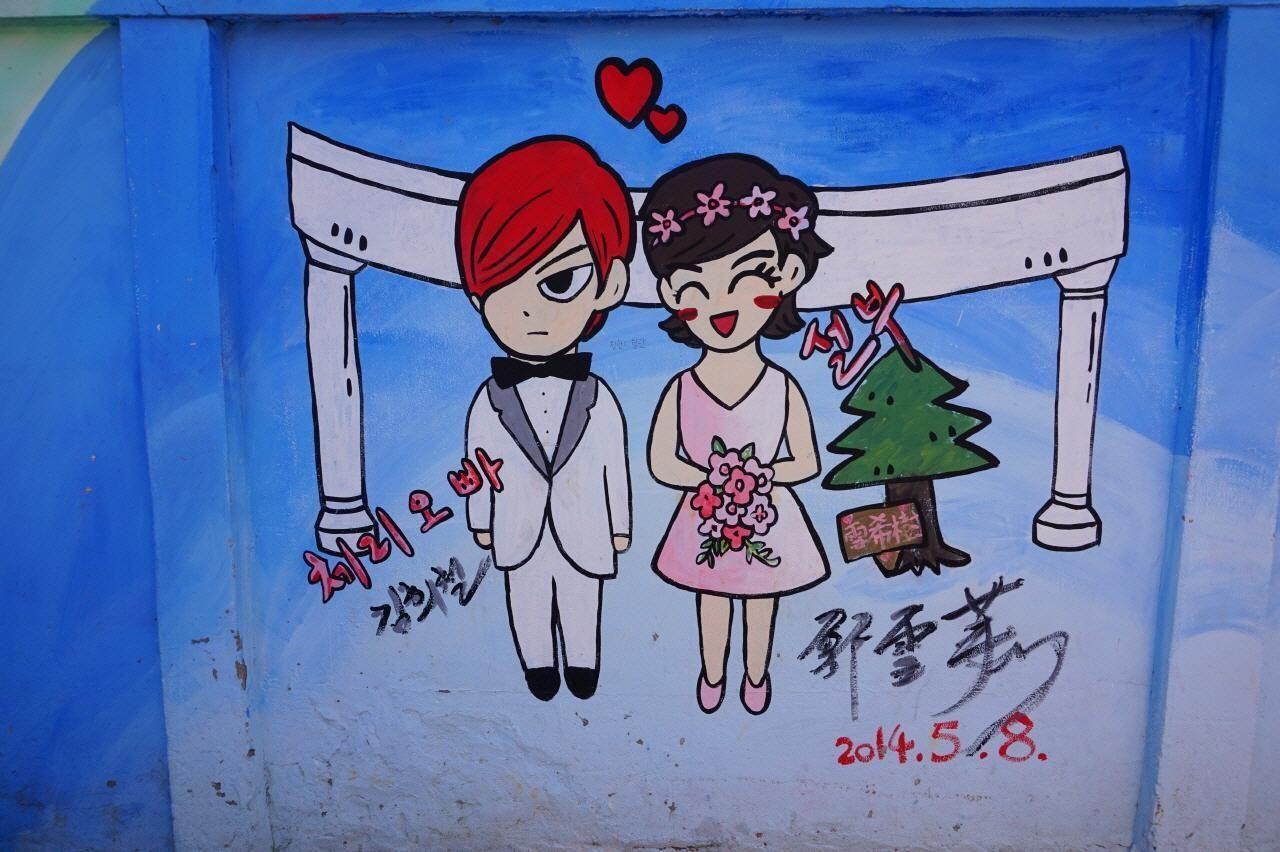 彩繪的壁畫，描繪了一對新郎新娘面帶笑容站在白色拱門下，色彩鮮明的社區壁畫。