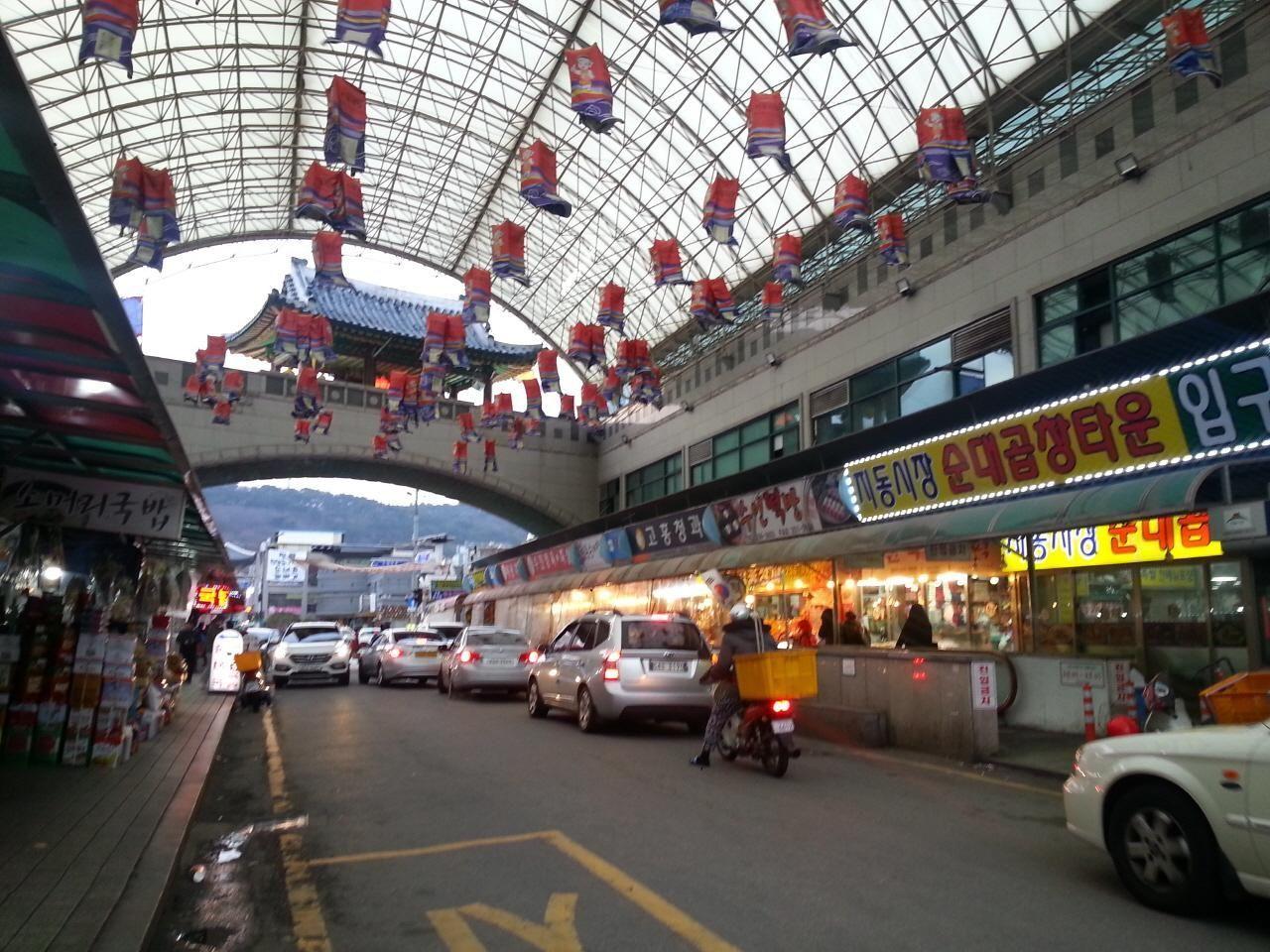 豬血腸村內的市場入口，商店牆上掛滿傳統燈籠，街道上車流不息，充滿市場氛圍。