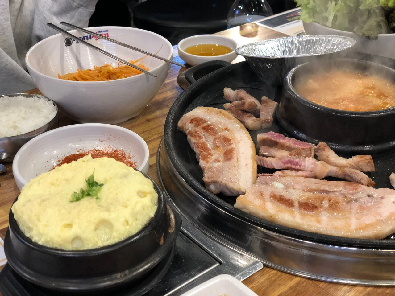 韓國燒肉餐，桌上擺放著烤肉、雞蛋蒸蛋等食物，配有金屬筷子和碗。