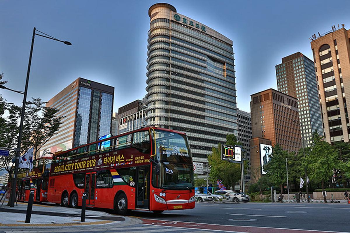 Seoul City Tour Bus cruising through bustling city streets against a backdrop of modern skyscrapers at twilight