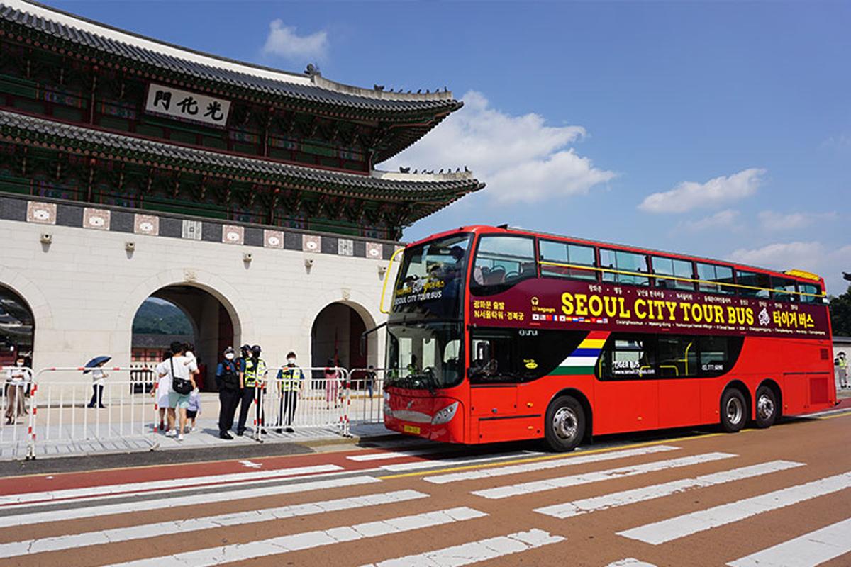Seoul City Tour Bus parked in front of Gwanghwamun Gate, showcasing a vibrant red double-decker bus under clear blue skies
