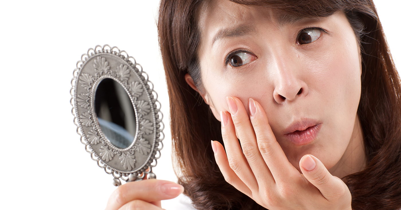 Woman holding an ornate mirror reflecting on her appearance, indicative of personal image concern prevalent in South Korean culture.