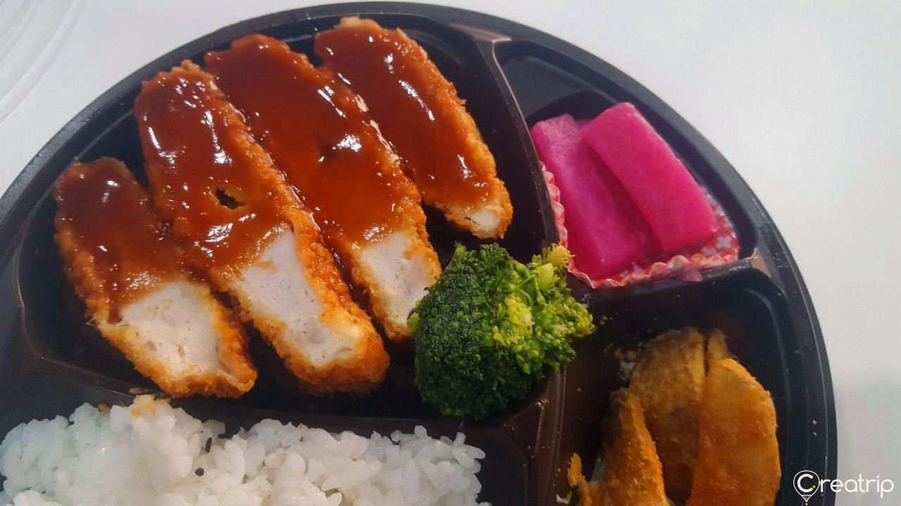 CU便利商店便当，特写猪排配菜，展示酱汁淋在猪排上，旁边有西餐风格的配料。