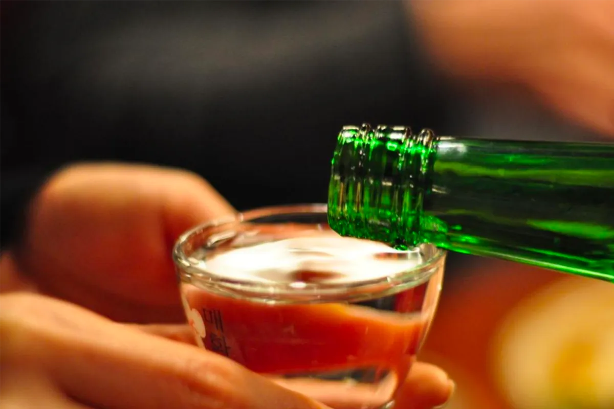 Detail of a person pouring soju into a glass in a Korean dining setting, a common pairing for Korean meals enjoyed by solo diners.
