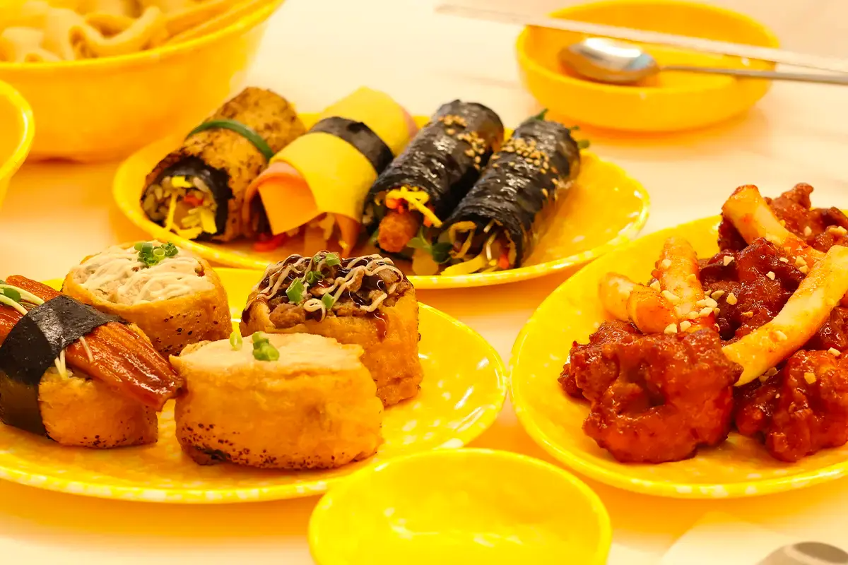 A colorful display of various Korean gimbap (rice rolls) and spicy dishes on yellow plates, typically found in Korean snack eateries.