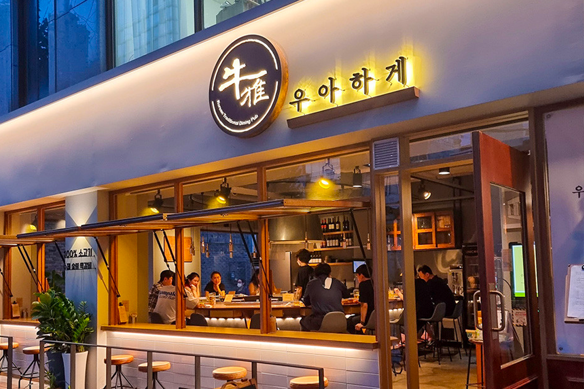 Exterior view of a Korean restaurant named 牛雅 featuring patrons enjoying an evening meal.