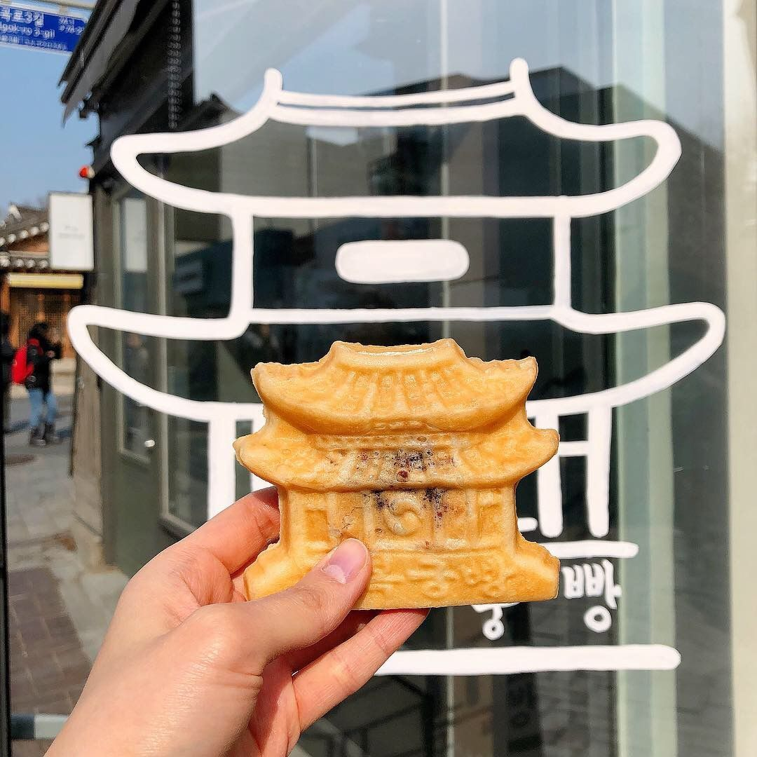 Hand holding a Gyeongbokgung-shaped pastry in front of the café window logo