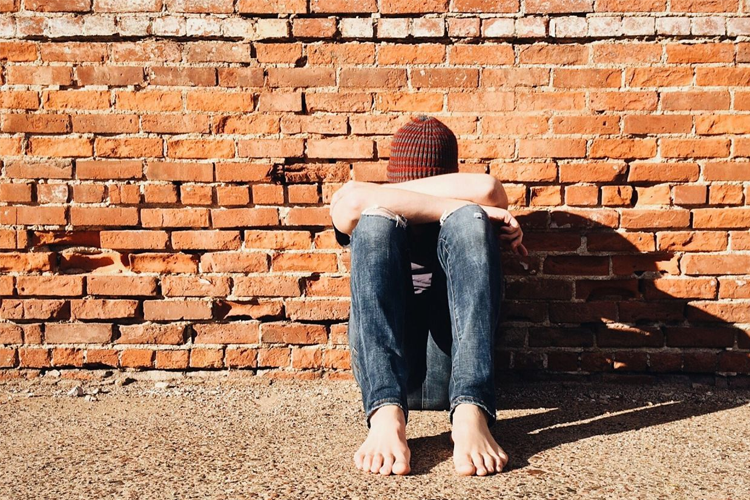 Person sitting alone against a brick wall, reflecting on themes of exclusion or feeling isolated from a cohesive group.