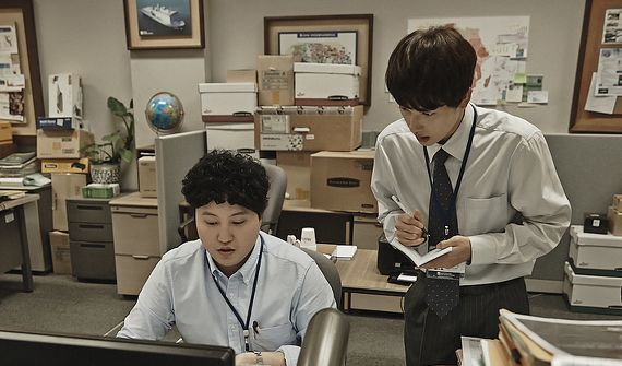 韓國辦公室內，一名穿著西裝的男子正在站立指導另一名坐著的男子，強調了韓國職場的階級文化，詮釋《未生》場景。