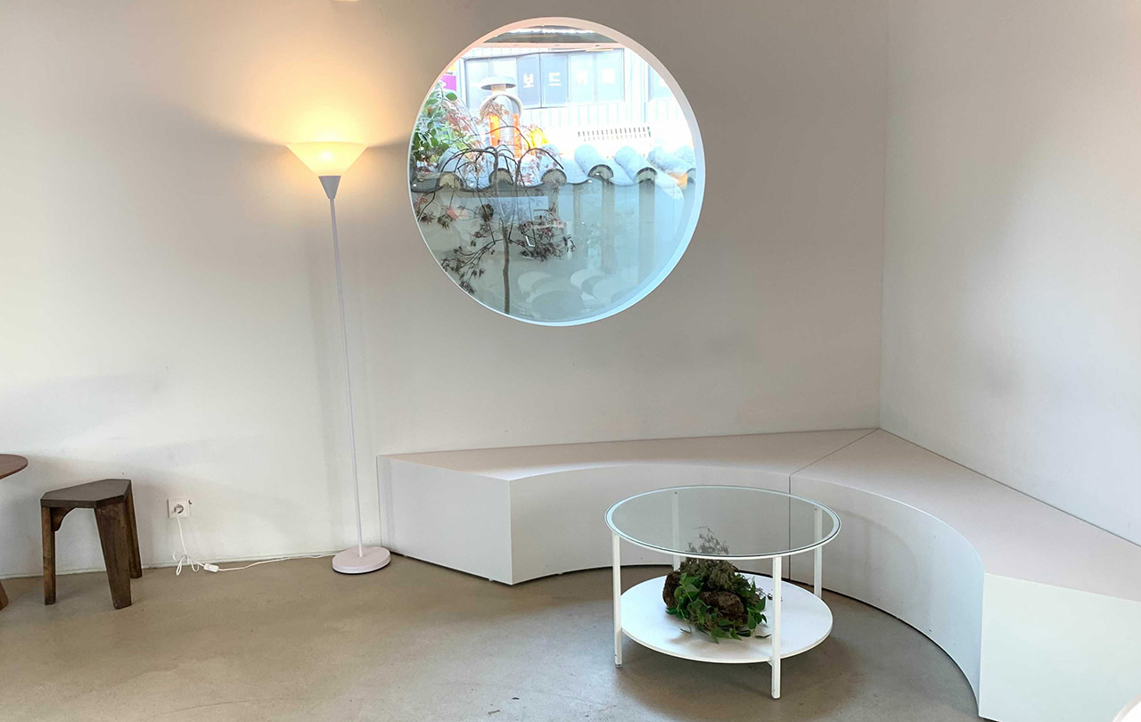 Minimalistic and modern white interior of Shinidoga cafe, featuring a rounded window and a cozy seating area.