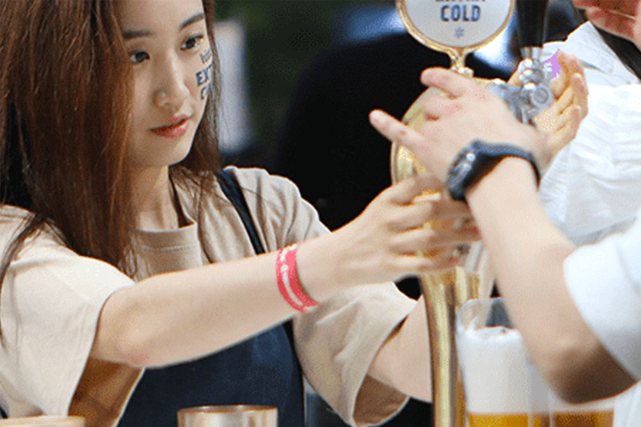 模糊面孔的顾客在酒吧酒桌上倒啤酒，展示韩国法律规定的实际成年人年龄和饮酒相关的合法年龄限制。