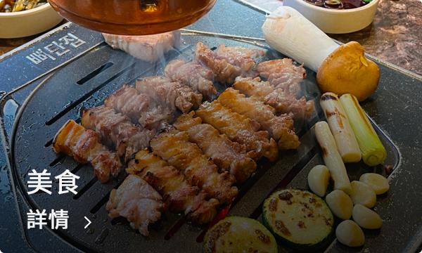 正正在韓國西村街頭市集的小攤檔，新鮮韓式美食正在料理中，畫面中的燒烤豬肉與蔬菜在燒烤架上發出誘人的金黃色澤，搭配着蒜頭與香菇，讓人垂涎三尺。