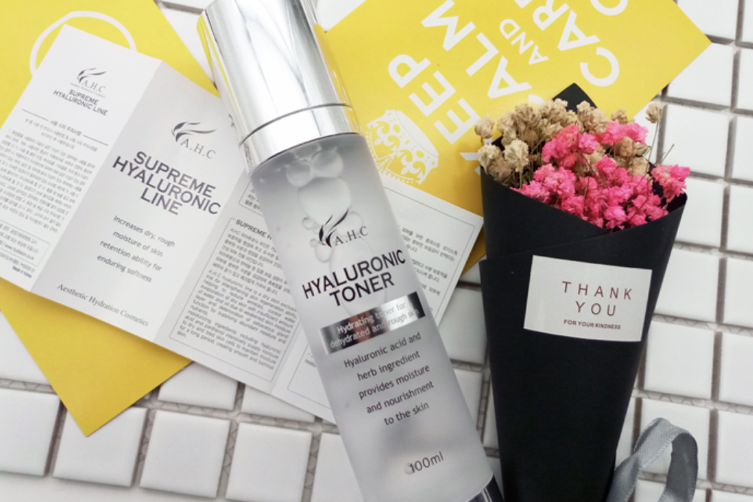 AHC Hyaluronic Toner bottle on a white tile surface alongside floral bouquet and product brochures.