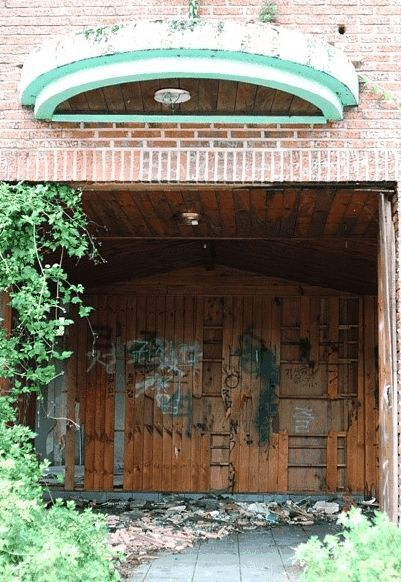 Mặt trước của ngôi nhà ma ám, phủ kín bởi cây cỏ và ván gỗ, trông tối tăm và ghê sợ - Neulbomgateun 늘봄가든 tại Chungcheongbuk-do, Hàn Quốc.