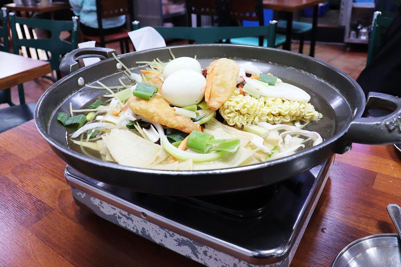 在放满食材的热锅中烹煮的韩国辣炒年糕锅，配有两颗白煮蛋，韩国蔬菜和拉面，与普通市场的辣炒年糕不同。新堂洞马福林辣炒年糕推荐。