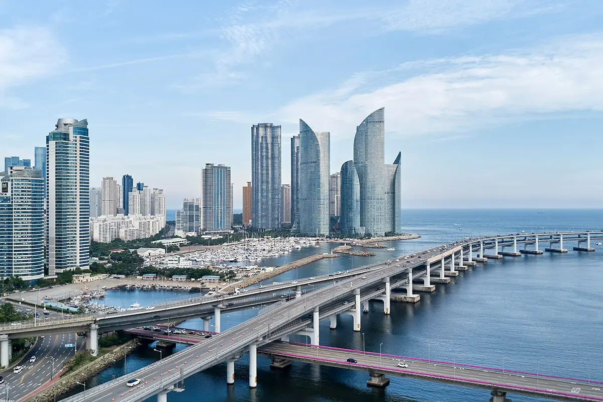 釜山城市景觀，全景顯示現代高樓大廈及海邊橋樑，畫面融入自然景象。