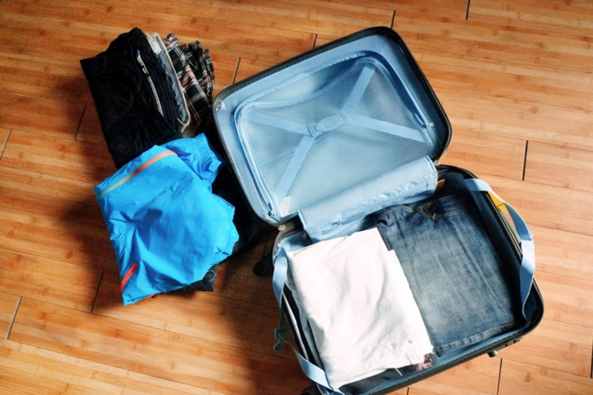 一個行李箱打開的上視圖，旁邊有摺疊整齊的衣物，背景是木製地板。