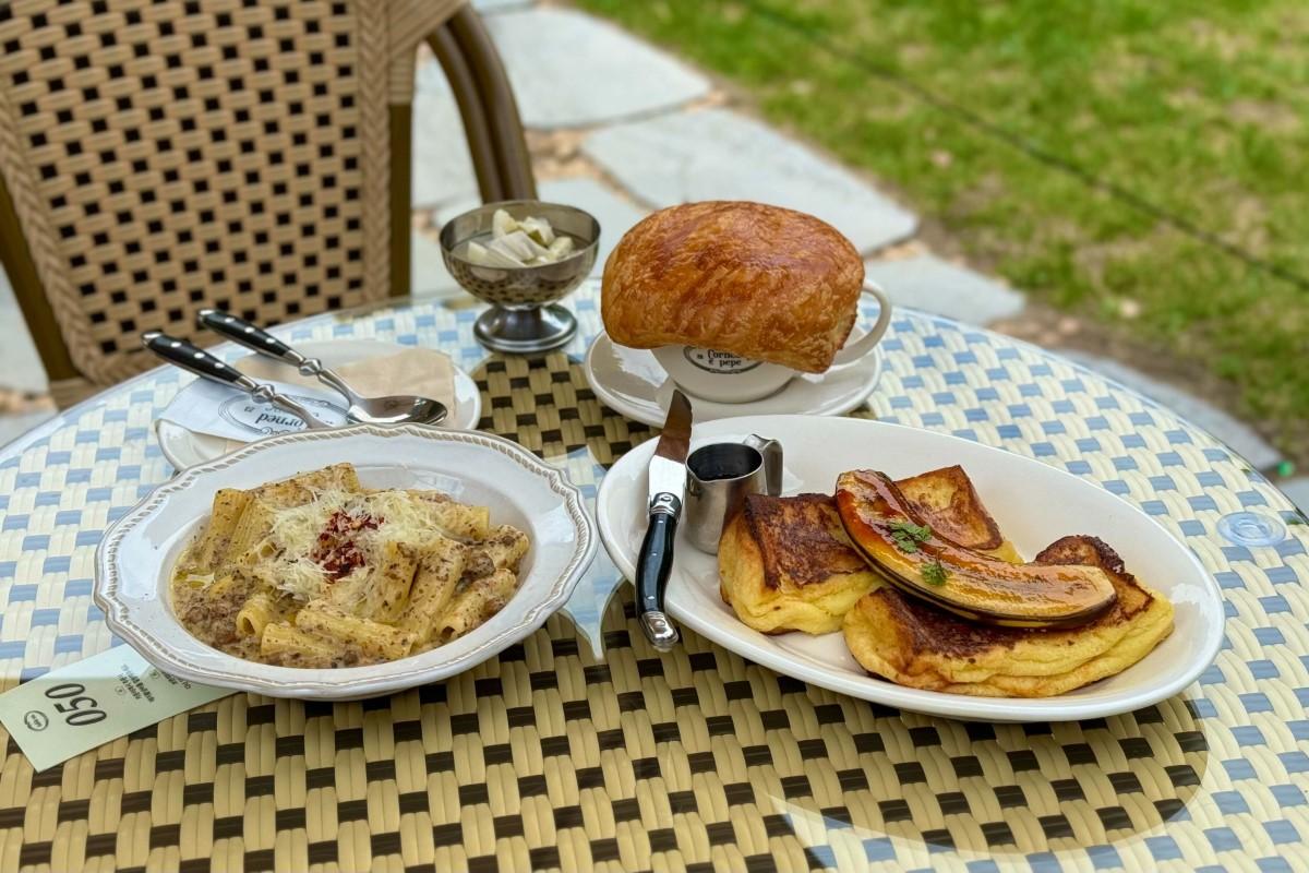 ソウルの人気カフェ『Corned e pepe』で提供されるパスタ料理とパン。テーブルセットが緑の庭園の中に置かれ、爽やかなブランチ体験を演出。