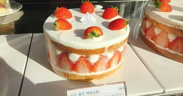 韩国蛋糕店,放在展示柜中的巧克力奶油蛋糕,每片切好放在白盘上,背景为现代风格的店铺装潢