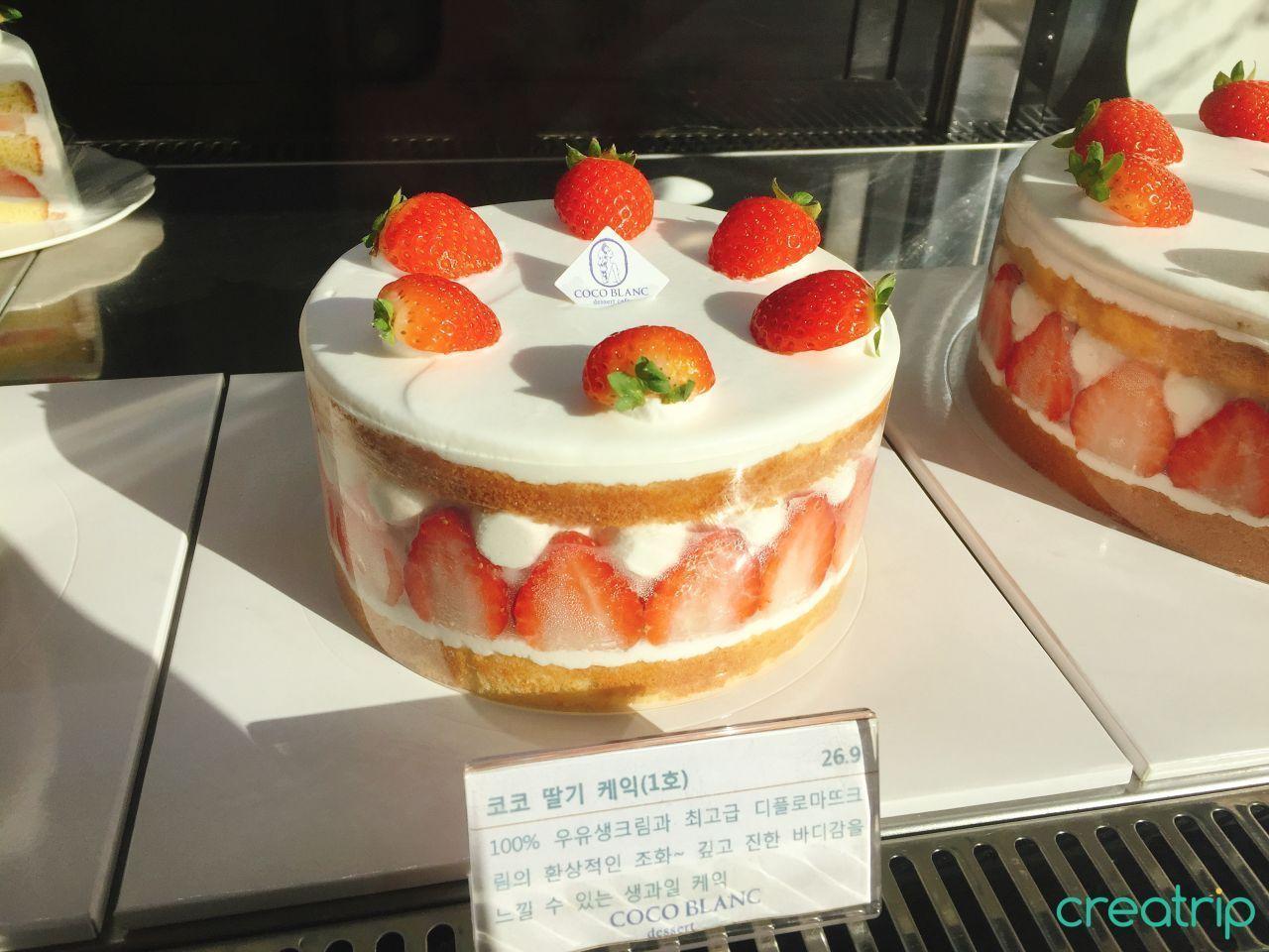 店铺内展示的整块水果奶油蛋糕,顶部饰有多颗草莓,背景为蛋糕展示柜