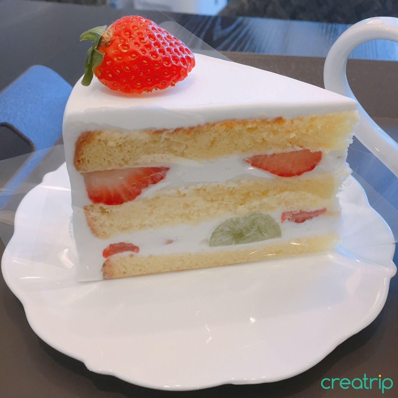 一片奶油草莓蛋糕放在白色盘子上,顶部装饰着一颗新鲜草莓