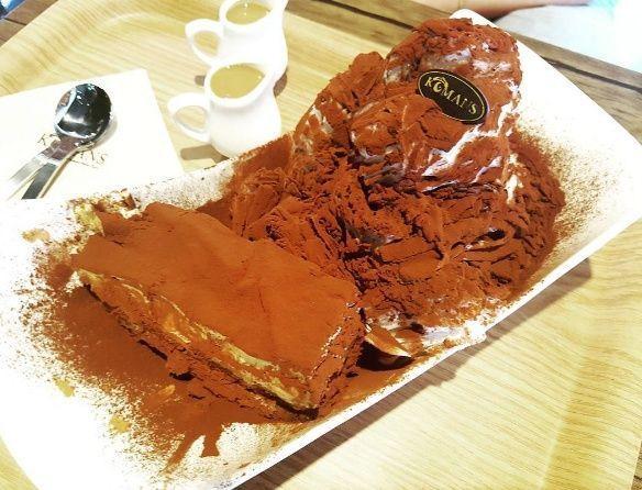 韩国甜品店 KOMANS 的提拉米苏,盛在大碟子中,撒有巧克力粉,旁有两小壶咖啡伴侣