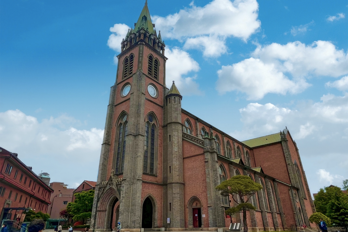 明洞大聖堂入口,台階兩側有鬱鬱葱葱的植物,上方可見具特色的教堂鐘樓,吸引遊客造訪。