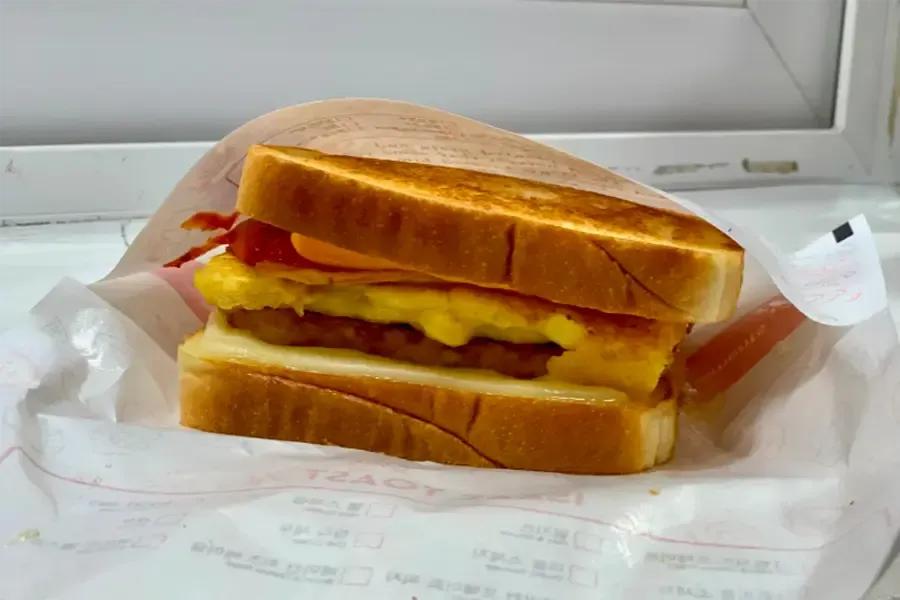 明洞のテイクアウト屋台で買える、ベーコン・ポテト・チーズ入りの焼きトースト。朝の観光に手軽でコスパ良く食べられる定番メニューの断面写真。