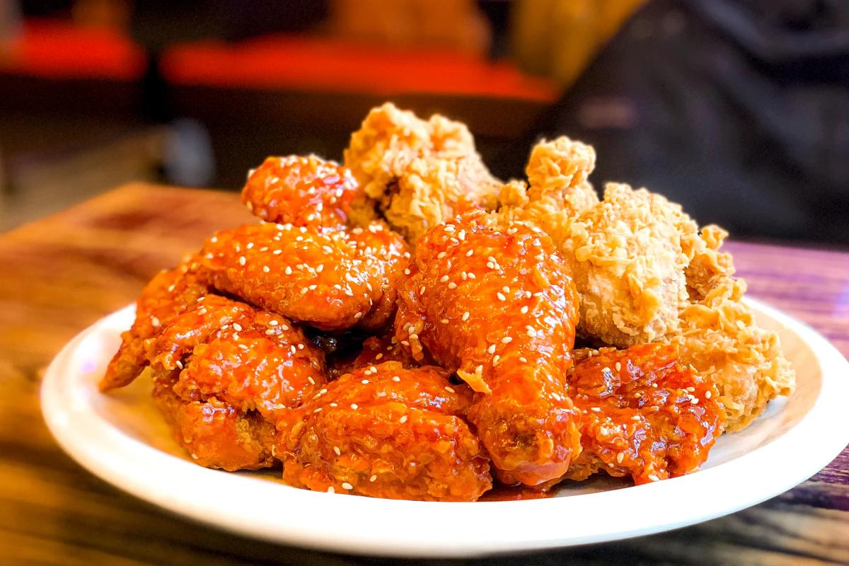 明洞のBBQチキン店で提供される、ヤンニョムソースと黄金オリーブのハーフ＆ハーフが盛られた揚げたてのチキンに白ごまとピクルスが添えられた一皿