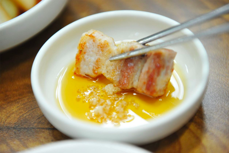 Crispy pork rind being dipped in soybean powder to highlight unique 요리 customs in Korean BBQ
