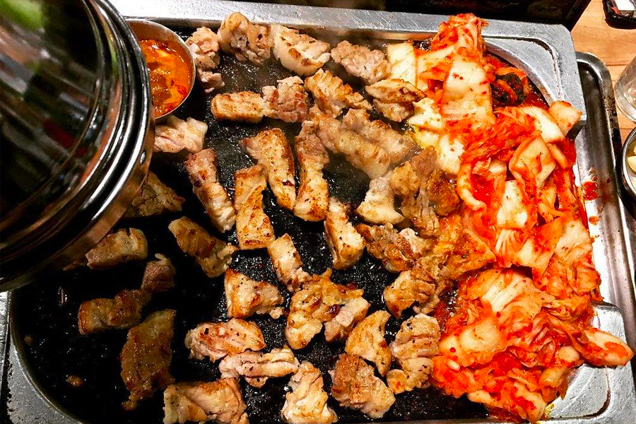 A grill loaded with pork belly pieces and various banchan, including kimchi, showcasing the Korean BBQ experience
