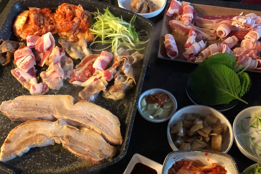 Korean BBQ setup with various banchan including perilla leaves, ready to complement pork belly 삼겹살