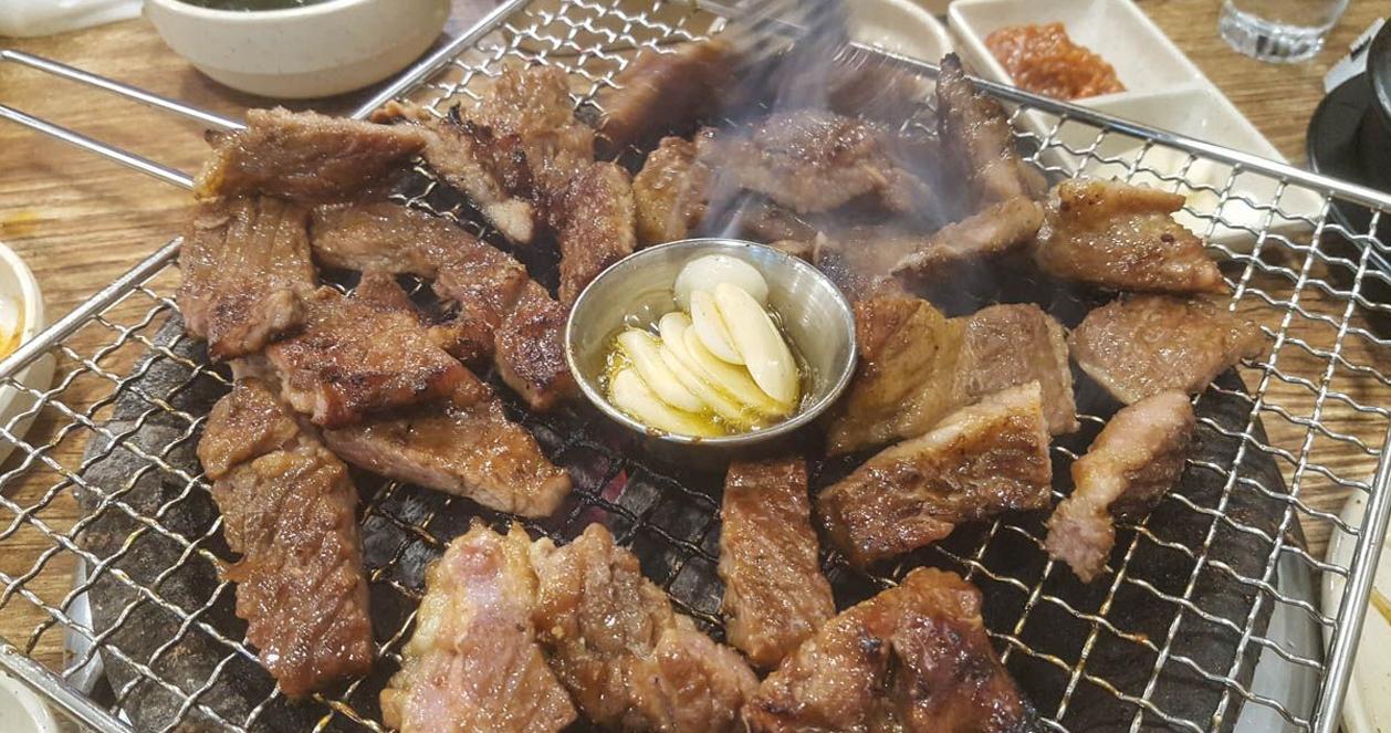 Thịt nướng Hàn Quốc được nướng trên vỉ với đĩa tỏi rang bên cạnh, tạo hương thơm hấp dẫn.