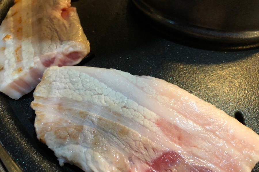 사진 of raw pork belly strips about to be grilled on a hot plate, part of a traditional Korean BBQ setup