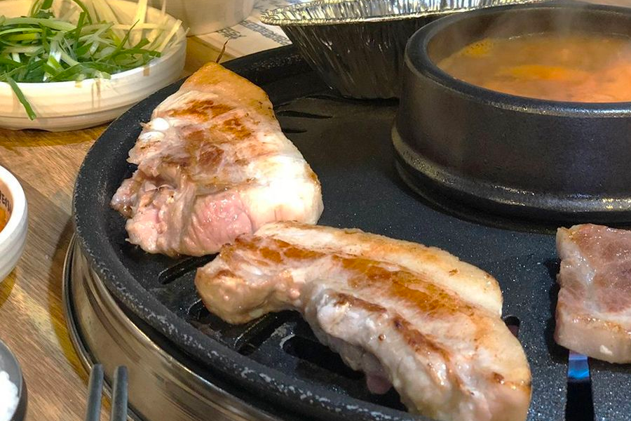 Close-up of 삼겹살 wrapped in lettuce with garlic and spicy sauce, showing a traditional Korean way to enjoy pork belly